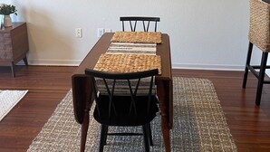 A dining area with a wooden table, black chairs, woven placemats, and a woven rug. A painting of a bug is on the wall. - Upscale condo centrally located in Baton Rouge!! (Baton Rouge)