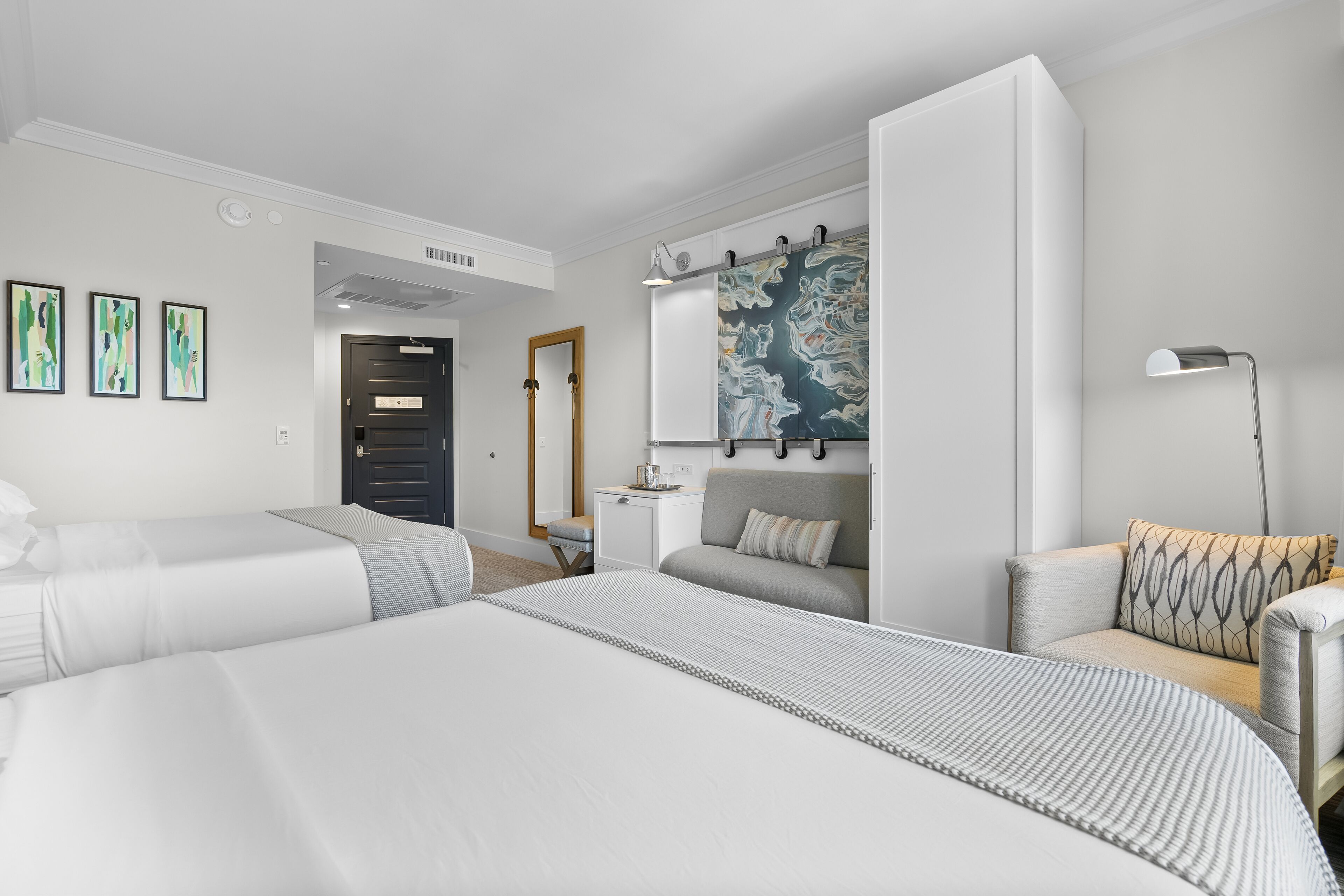 A modern hotel room with two beds, a sofa, a desk, and a large abstract painting.