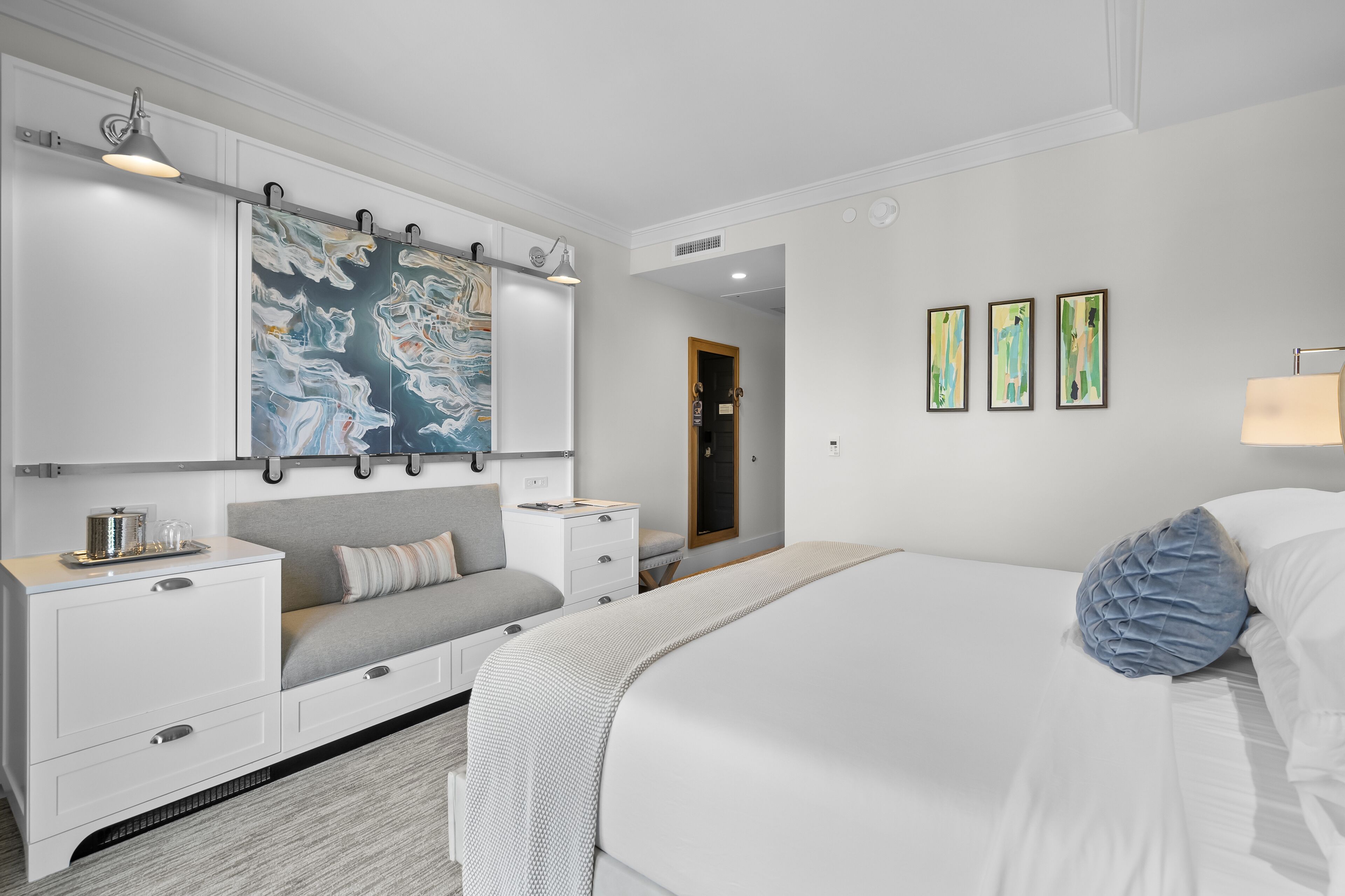A modern bedroom with a large bed, a bedside table, a nightstand, a dresser, and a large abstract painting on the wall.