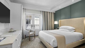 A hotel room with a bed, a desk, a chair, a TV, and a window with curtains.