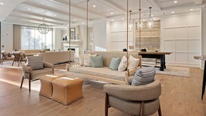 A spacious living area with a sofa, ottoman, and chairs, a dining area with a table, and a kitchen in the background.