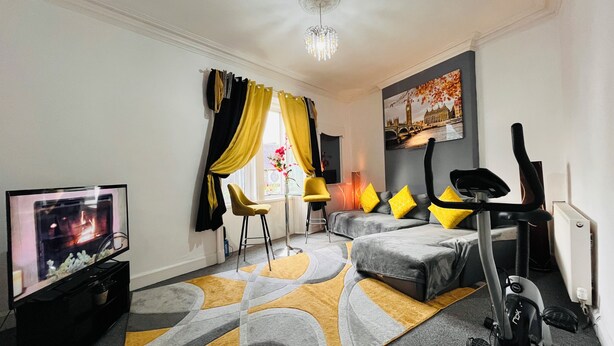 A modern living room with a TV, exercise bike, and a sofa with yellow cushions.