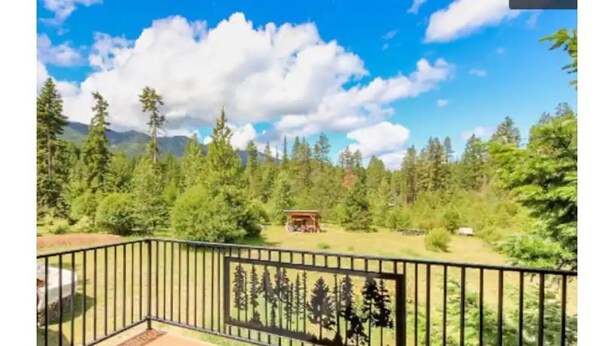 A wooden deck with a black metal railing, overlooking a forested area with a small wooden structure in the distance. - Luxury Cabin in Recreation Paradise! Close to everything: Nature, Food, Suncadia (Cle Elum)