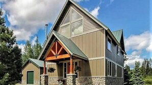 A two-story house with a stone foundation, a large front porch with wooden beams, and a green door. - Luxury Cabin in Recreation Paradise! Close to everything: Nature, Food, Suncadia (Cle Elum)