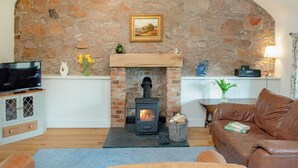 A cozy living room with a stone wall, a fireplace, a television, and a brown leather sofa. - 2 bedroom accommodation in Withleigh, near Tiverton (Withleigh, near Tiverton)