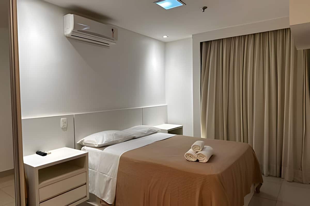 A modern hotel room with a single bed, a bedside table, a nightstand, and a large window with curtains.