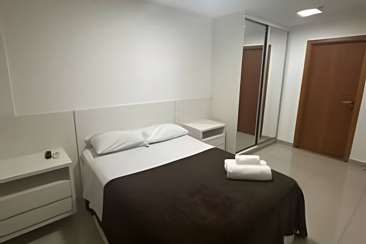 A modern hotel room with a bed, bedside tables, a mirror, and a wardrobe.