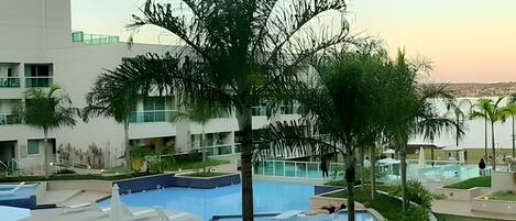 A modern hotel with a large pool area, palm trees, and a view of the surrounding landscape.