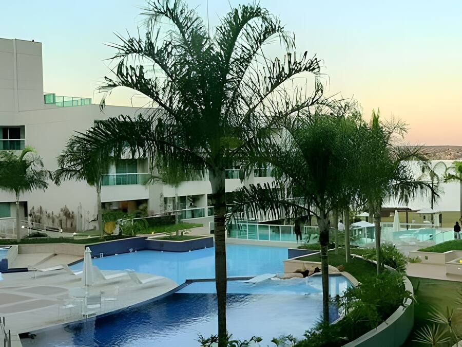Un hotel moderno con un'ampia area piscina, palme e vista sul paesaggio circostante.