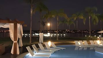 A poolside area with lounge chairs and palm trees at night.