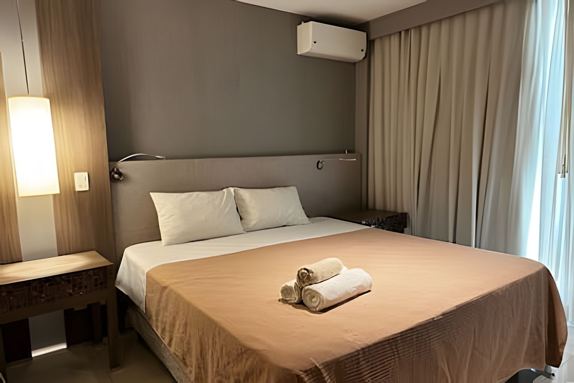 A hotel room with a large bed, a bedside table, a lamp, and a window with curtains.
