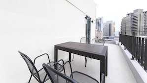 A balcony with a table and chairs, a white wall, and a view of city buildings. - BONATREE HOTEL (Busan)