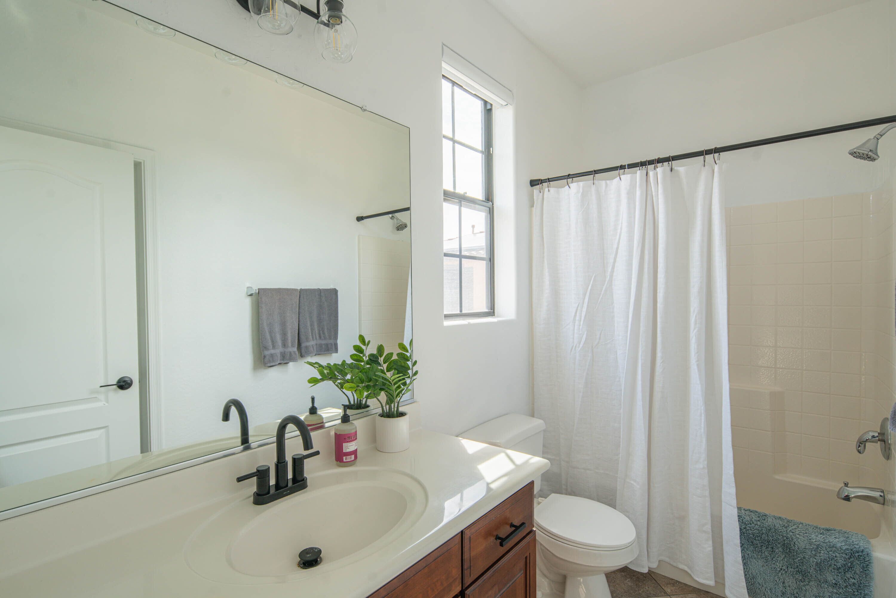 Un baño con lavamanos blanco, espejo, inodoro, ducha y ventana.