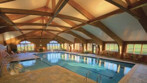 Une piscine intérieure avec des poutres en bois, des chaises longues et une vue sur l’extérieur.