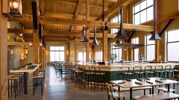 Un restaurant spacieux avec de hauts plafonds en bois, de longues tables et des lampes suspendues.