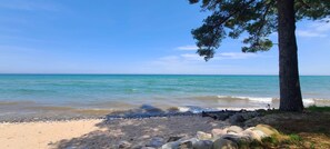 Ein Strand mit klarem, blauem Wasser, einem Sandufer und einer Baum.