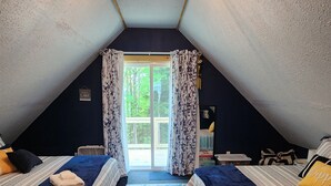 Un dormitorio acogedor en el ático con dos camas, un ventanal con cortinas y una lámpara en el techo.