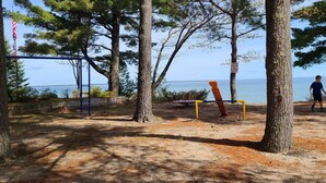 Un parque con árboles, un área de juegos y un banco junto al agua.