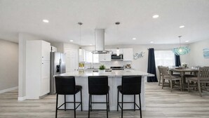 Una cocina moderna con una isla central, taburetes de bar y un comedor con candelabro.