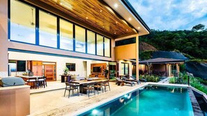 Una casa moderna con piscina, mobiliario exterior y un amplio ventanal con vistas a un paisaje exuberante.
