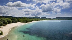 Una playa con aguas turquesas cristalinas, una orilla arenosa y colinas verdes exuberantes al fondo.