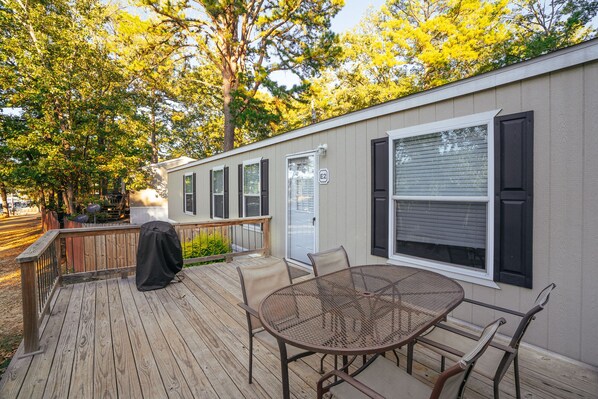 A covered outdoor patio with a metal table and chairs, a grill, and a deck railing.