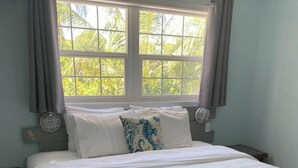 A neatly made bed with white and pink linens, a window with curtains, and a view of palm trees outside. - This is a great vacation home with oceans views  (George Town)