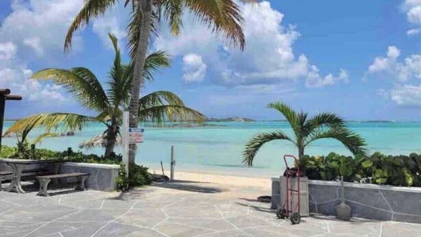 A paved patio with stone tiles, palm trees, and a view of a beach and turquoise waters. - This is a great vacation home with oceans views  (George Town)