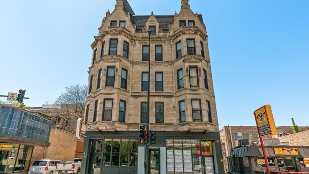 Un edificio histórico con entrada en esquina, ventanas amplias y una señal de calle visible.