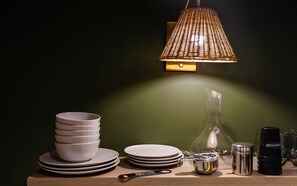 A table with stacked plates, a glass pitcher, a metal container, and a black bottle, all under a textured lamp. - The Neighborhood Hotel Grand Beach Suite 12 - Three Bedroom (Grand Beach)