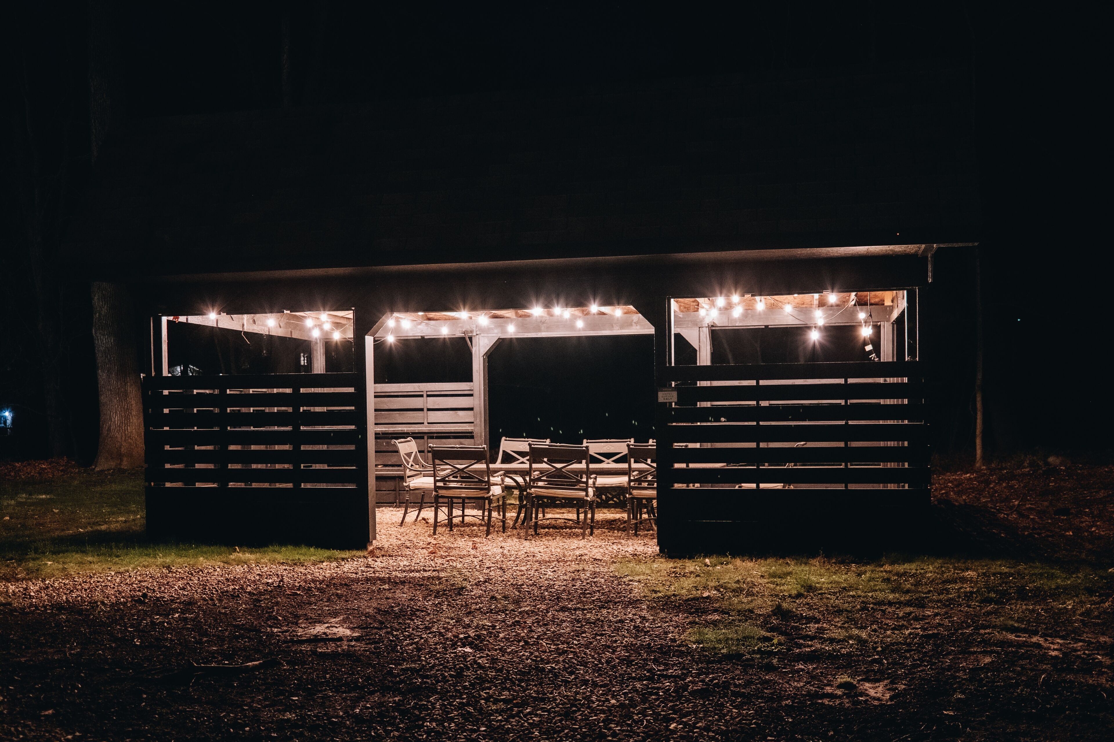 Un área de estar al aire libre techada con luces colgantes, bancos de madera y una mesa.