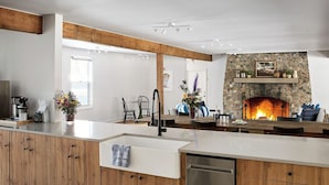 A modern kitchen with a stone fireplace, wooden cabinets, and a central island.