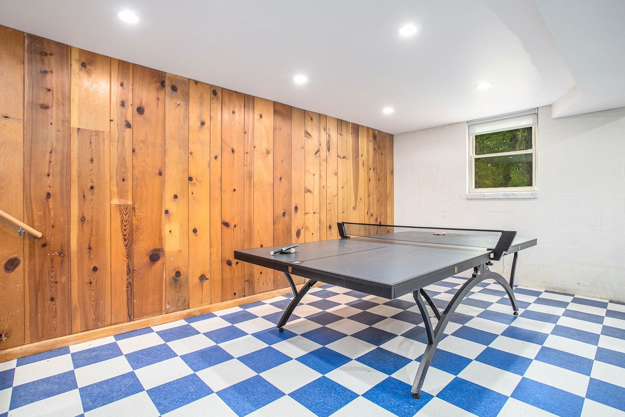 Une table de ping-pong dans une pièce dont le sol est à carreaux et les murs sont recouverts de panneaux de bois.