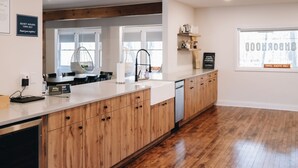 A modern kitchen with wooden cabinets, a white countertop, and a built-in dishwasher. There is a hanging chair near the window and a sign indicating quiet hours.