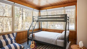 A bunk bed room with a view of trees through large windows, a guitar, and a wicker chair. - The Neighborhood Hotel Grand Beach Suite 1 - Three Bedroom (Grand Beach)