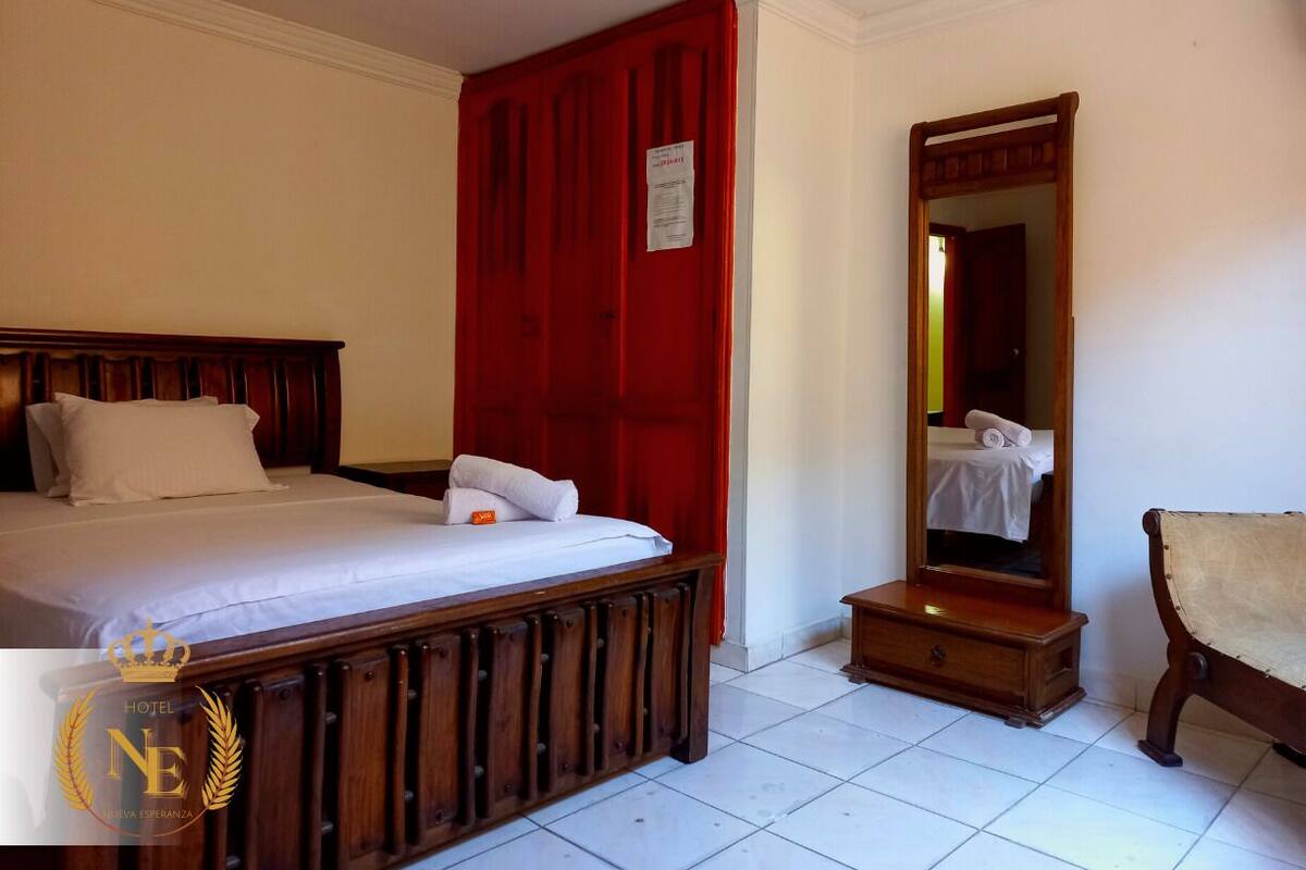 Une chambre d’hôtel avec un lit en bois, un rideau rouge, une commode en bois et un miroir.
