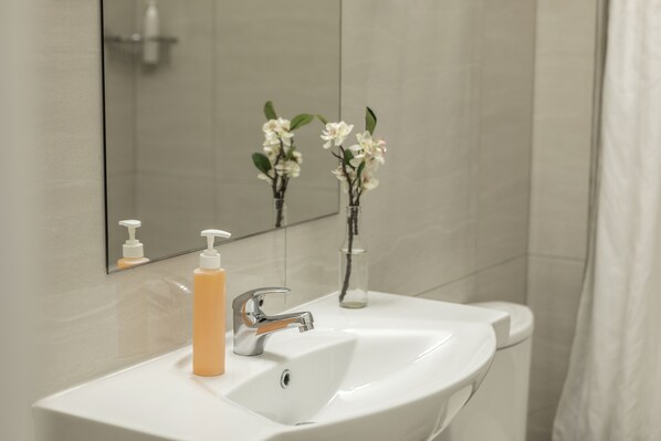 A bathroom with a white sink, a mirror, and a glass vase with flowers.