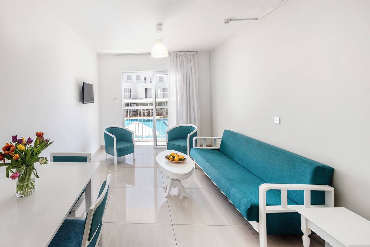 Ein modernes Wohnzimmer mit einem türkisfarbenen Sofa, einem weißen Couchtisch und türkisfarbenen Sesseln. Vor dem Sofa steht ein kleiner weißer Tisch.