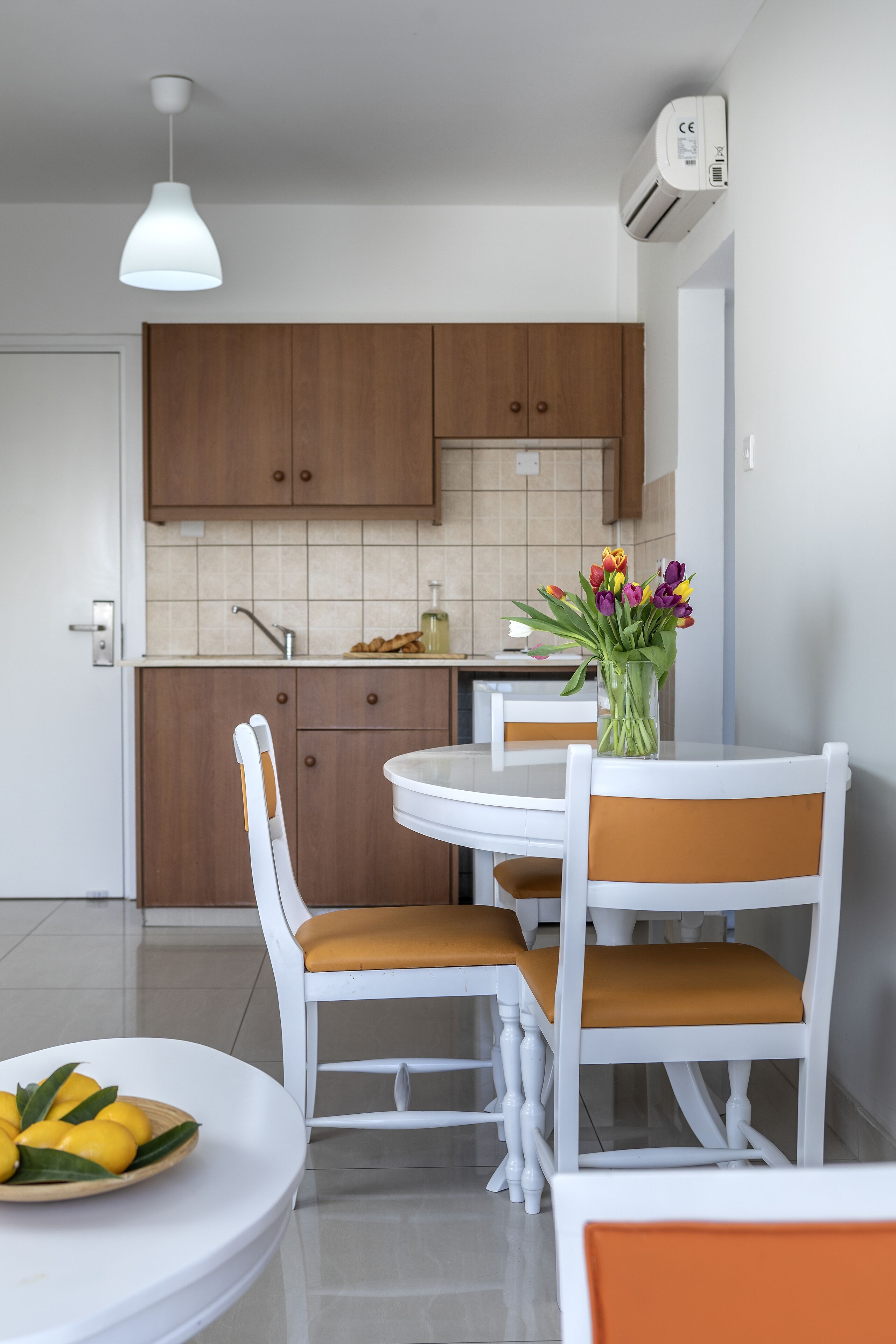 Et moderne køkken med træskabe, et hvidt spisebord med to stole og en vase med blomster på bordet.