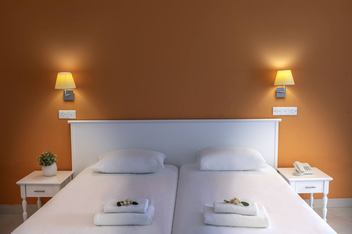 Ein Doppelbett mit weißen Bettwäsche, zwei Nachttische, ein kleiner Topfpflanze und ein Nachttischtelefon.