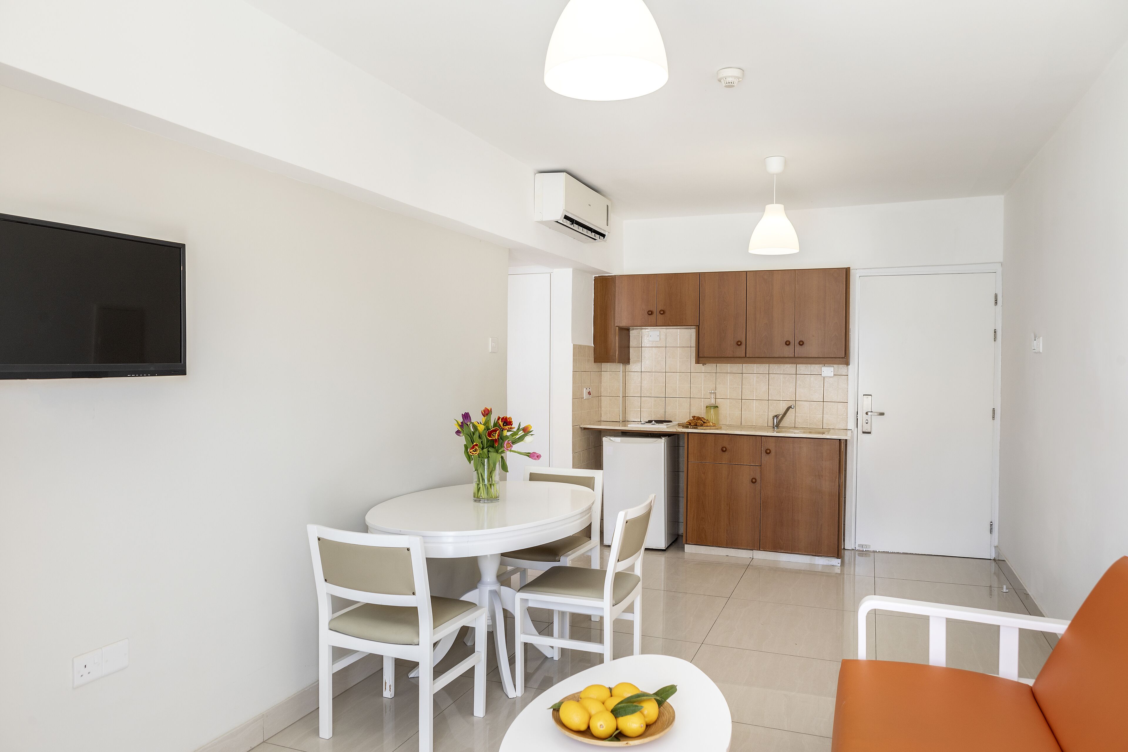 Una cocina moderna con armarios blancos, un comedor con una mesa y sillas blancas, y una pequeña silla naranja.