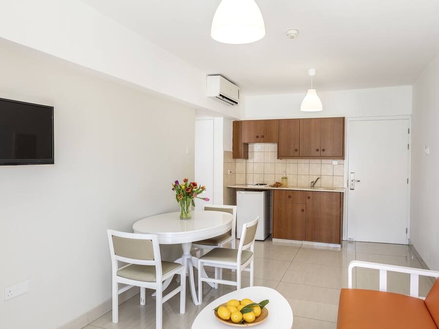 Una cocina moderna con armarios blancos, un comedor con una mesa y sillas blancas, y una pequeña silla naranja.