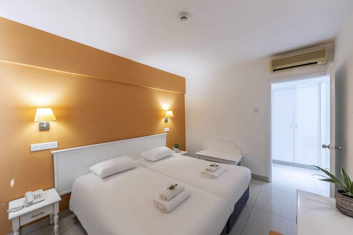 Ein Hotelzimmer mit zwei Betten, einem Nachttisch mit Lampe, einem Telefon und einer Pflanze.