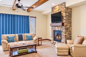 A living room with a stone fireplace, leather sofas, a coffee table, and a ceiling fan.