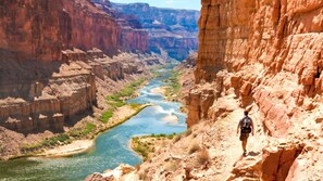 Un canyon avec une rivière, un randonneur et un terrain rocheux.