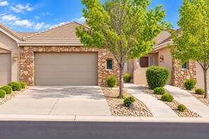 A residential house with a stone facade, a garage, and a well-maintained front yard with trees and shrubs.