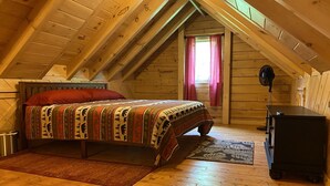A cozy attic bedroom with a wooden ceiling, a bed with patterned bedding, a small rug, and a dresser. - Log cabin~hike, hunt, ski,with direct snowmobile trail access and outdoor sauna. (Upton)