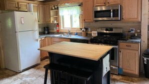 A kitchen with wooden cabinets, a stainless steel refrigerator, a microwave, a stove, and a sink. - Log cabin~hike, hunt, ski,with direct snowmobile trail access and outdoor sauna. (Upton)