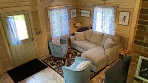 A cozy cabin interior with a wooden interior, a beige sofa, a blue armchair, and a small table. - Log cabin~hike, hunt, ski,with direct snowmobile trail access and outdoor sauna. (Upton)