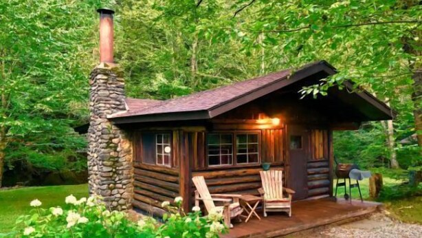 Eine rustikale Holzhütte mit einem Steinkamin, Holzwänden und einer Veranda mit Sitzgelegenheiten.